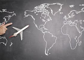 Top view of miniature airplane placed on over gray world map with crop hand of anonymous person indicating direction representing travel concept